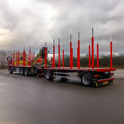 Roter Holztransport-LKW mit Langholzanhänger, roten Rungen und Ladekran auf nasser Straße.