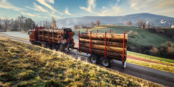Truck with DOLL center-axle trailer drives along a narrow country road between meadows and fields at dawn