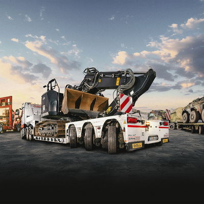 Heavy haulage with low-loaders carrying construction and military vehicles under a dramatic sky.