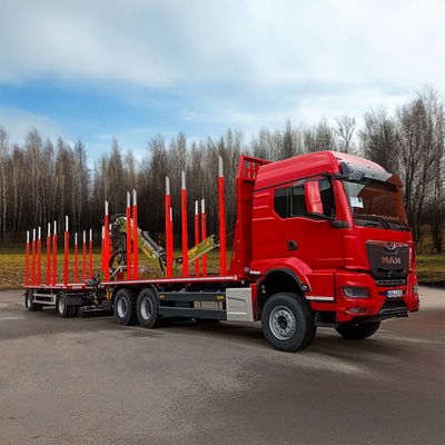 Roter Holztransport-LKW mit DOLL Drehschemelanhänger, roten Rungen und Ladekran vor bewaldeter Landschaft.